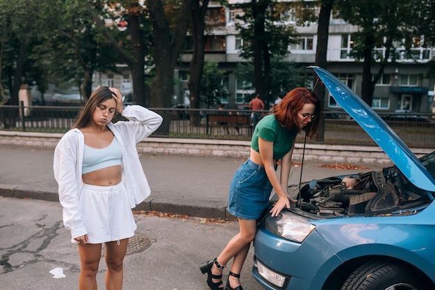 Two women with broken car on the road Open hood