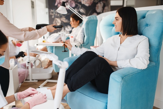 Two women with champagne, pedicure procedure in beauty salon.