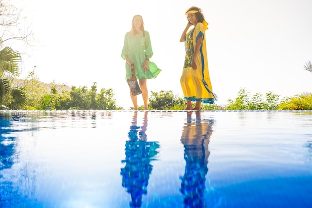 Two women with colorful dress posing next to an outdoor pool