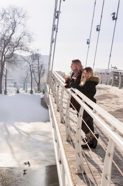 two women with cups of coffee on the bridge in winter