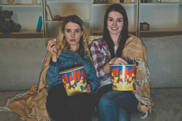 Две женщины с попкорном смотрят фильм на диване
