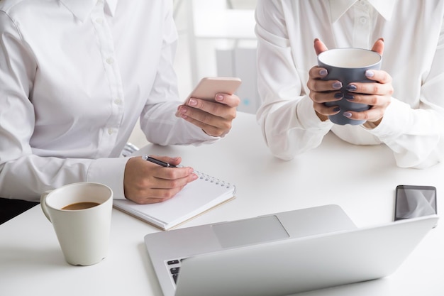 Two women working in office with coffee and notebook