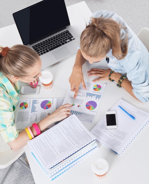 Two women working together at office, sitting on the desk