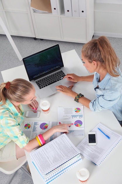 Two women working together at office sitting on the desk