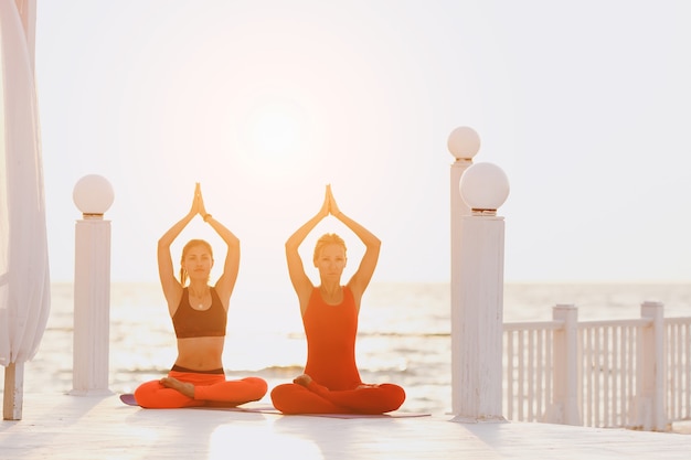 A two women do yoga at sunrise near the sea