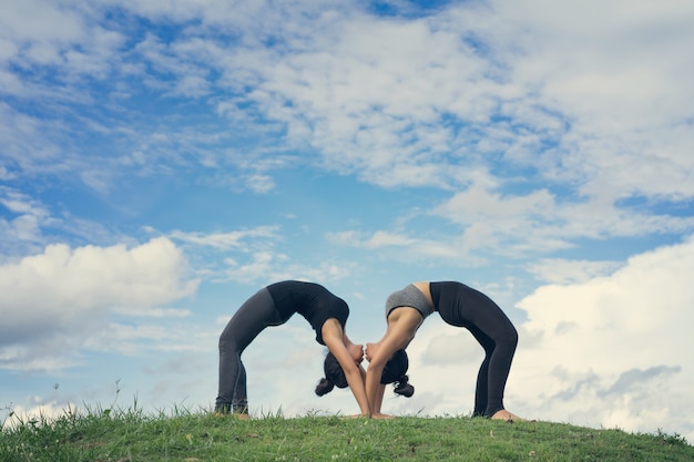 Due donne fanno yoga urdhva dhanurasana o chakra-asana nel parco sul bellissimo cielo di giorno soleggiato.