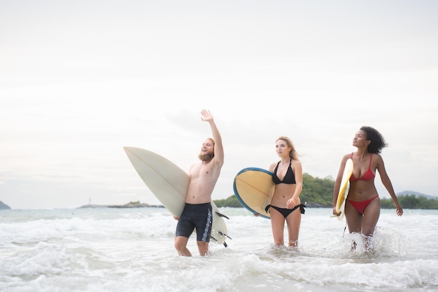 Photo two women and young man holding surfboards ready to walk into the sea to surf