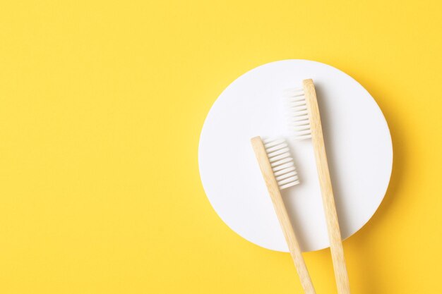 Two wooden bamboo eco friendly toothbrushes on round podium on yellow background