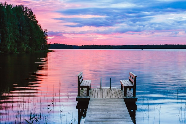 写真 フィンランドの日没時に湖を見下ろす木製の桟橋にベンチ2つの木製の椅子