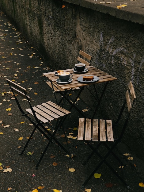 Two wooden chairs with a table with two cups of coffee and a cupcake on it.