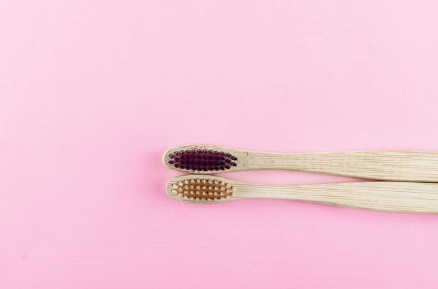 Two wooden eco brushes with natural bristles on pink paper background.