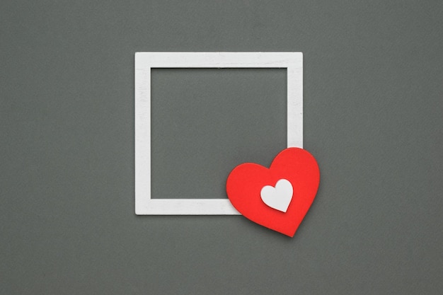 Two wooden hearts and a white wooden frame on a gray background. The concept of Valentine's Day. Flat lay.