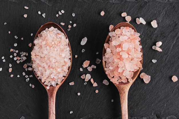 Photo two wooden spoons lying on a slate are filled with pink salt
