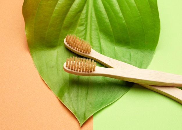 Two wooden toothbrushes on a green orange background, plastic rejection concept