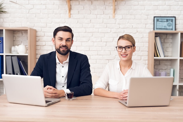 Two workers are sitting at table and working with a laptop.