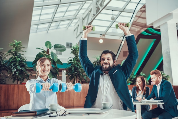 Two workers exercising with dumbbells in office.