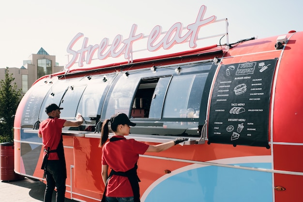 Foto due operai di un camion di cibo che puliscono un furgone rosso al mattino