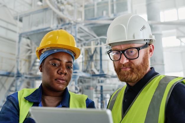 Two workers of modern factory looking through information at tablet screen