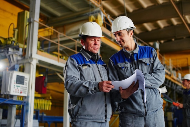 Two workers in overalls holding documents and looking at them in the premises of the factory