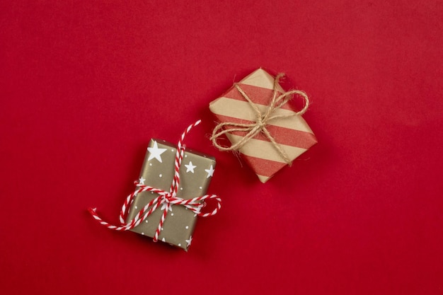 두 개의 포장된 크리스마스 선물과 선물 상자는 줄무늬와 별과 복사 공간이 있는 빨간색 배경에 공예 종이 상단 보기로 포장되어 있습니다.