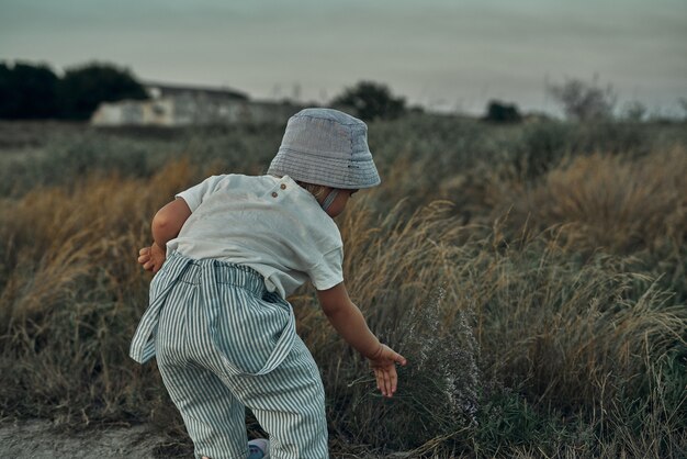 帽子をかぶった2歳の子供が田舎道を歩く