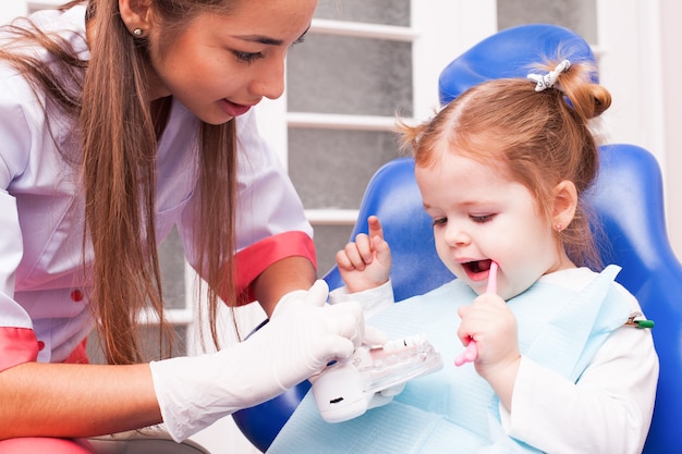 2歳の女の子が歯科医院で手に歯ブラシで歯を磨くことを学んでいます