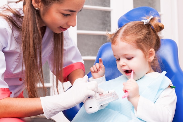 Two years old girl is learning to brush her teeth with toothbrush in hand in the dental office