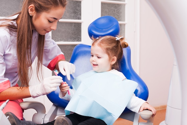 Una bambina di due anni sta imparando a lavarsi i denti con lo spazzolino in mano nello studio dentistico