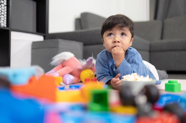 Two years old mexican baby boy eating popcorn on messy room