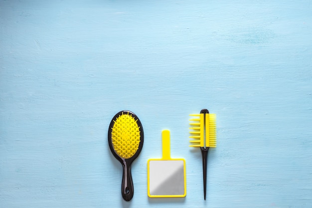 Due spazzole di cresta pettine capelli gialli con manico per tutti i tipi e specchio isolato su spazio blu copia. posa piatta minimalista femminile