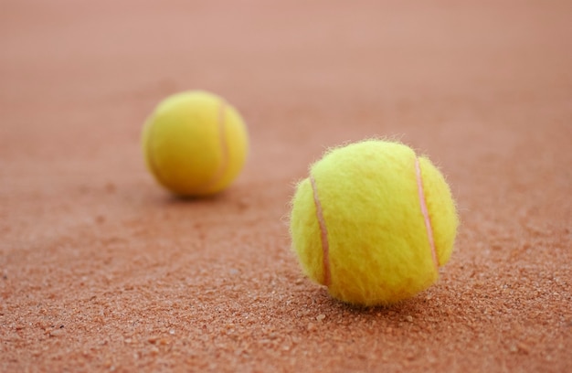 Two yellow tennis balls on the floor of the clay court.