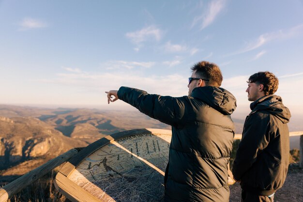 Photo two young adventurers bundled up on top of a mountain looking at a lake and mountains