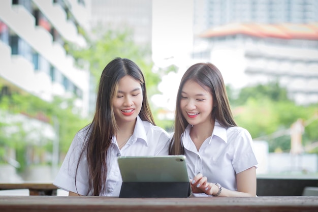 Two young Asian girls students are consulting together and using a tablet to search information