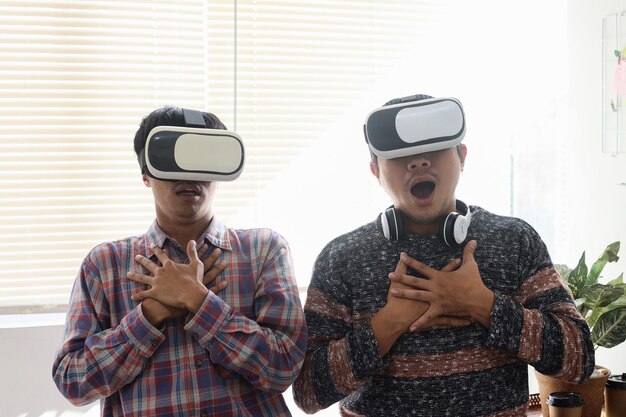 Two young Asian men showing shocked expression when playing game using virtual reality headset