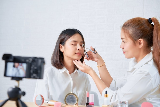 Two young Asian woman beauty vlogger video online is showing make up on cosmetics products and live video on digital digital camera.