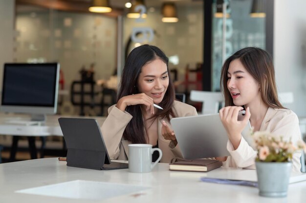 사진 두 젊은 아시아 여성이 태블릿을 사용하여 사무실에서 개념 작업에 대해 토론합니다.
