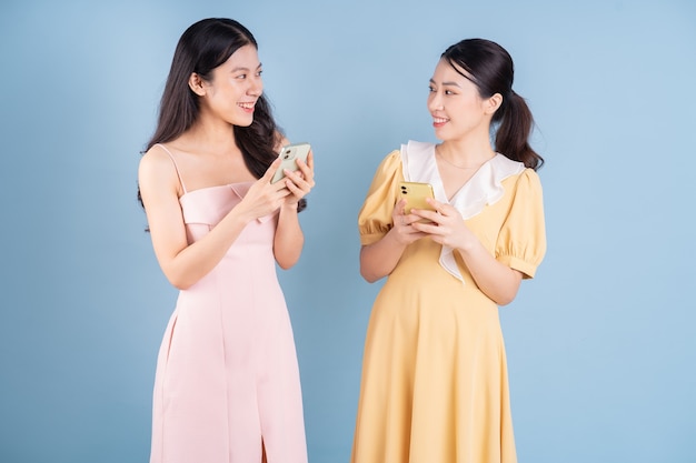 Two young Asian woman holding smartphone on blue background