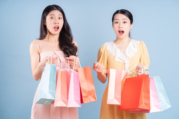 Two young Asian women holding shopping bag on blue background