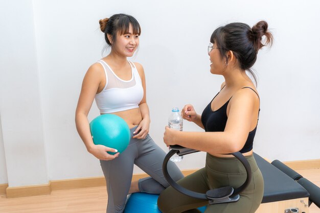 Two young Asian women talking while taking a water break during their pilates fitness exercise