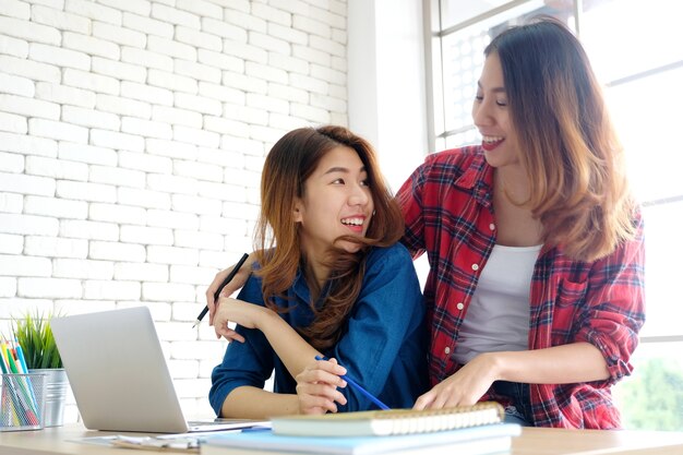 Two young asian women working with laptop computer at home office with happiness