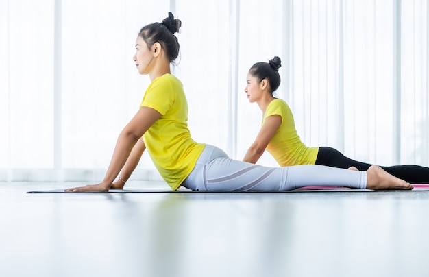 Two young Asian women workout practicing yoga in yellow dress or pose with a trainer and practice meditation wellness lifestyle and health fitness concept