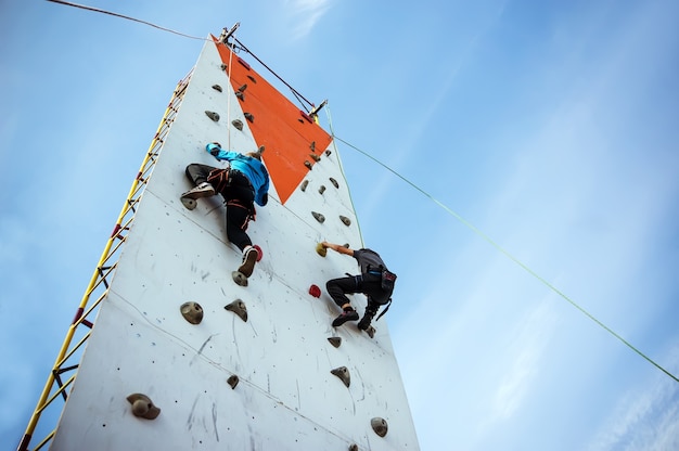 Two young athlete's compete in climbing a vertical climbing wall on the sky background