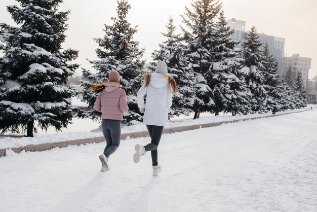 Two young athletic girls running in the park on a sunny winter day. A healthy way of life.