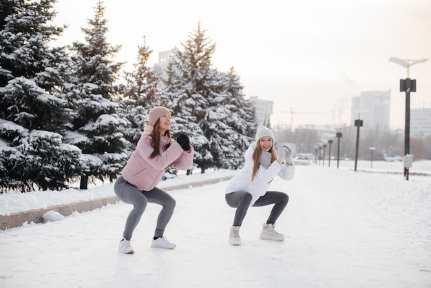 Two young athletic girls do a warm-up before running on a sunny winter day. A healthy way of life.