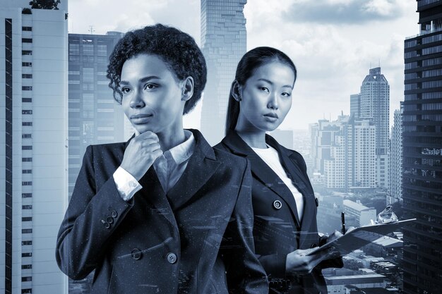 Two young attractive businesswoman in suits dreaming about new career opportunities after MBA graduation Concept of multinational corporate team Bangkok on background Double exposure