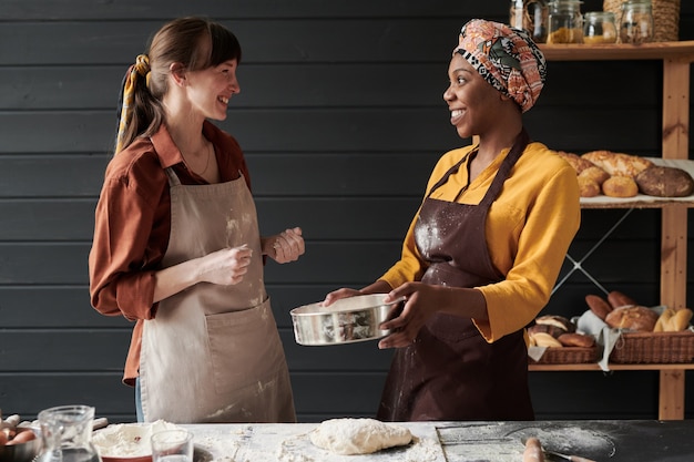 Photo two young bakers in aprons baking the bread together while standing in the kitchen