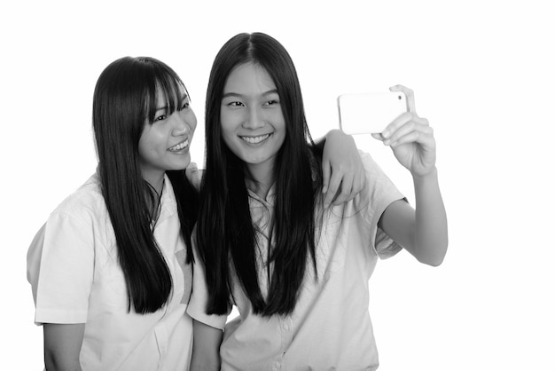 Two young beautiful asian teenage girls together isolated against white wall in black and white