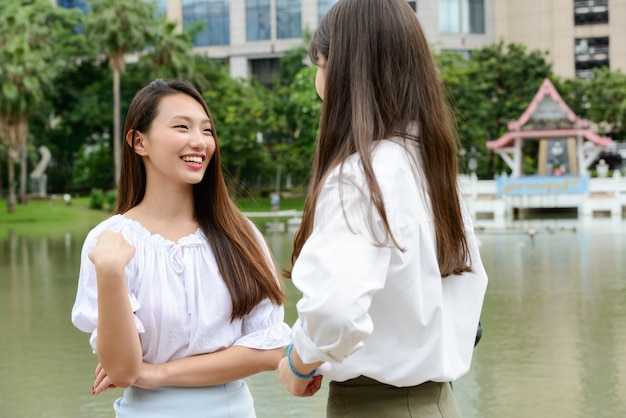 Two young beautiful Asian teenage women talking at the park