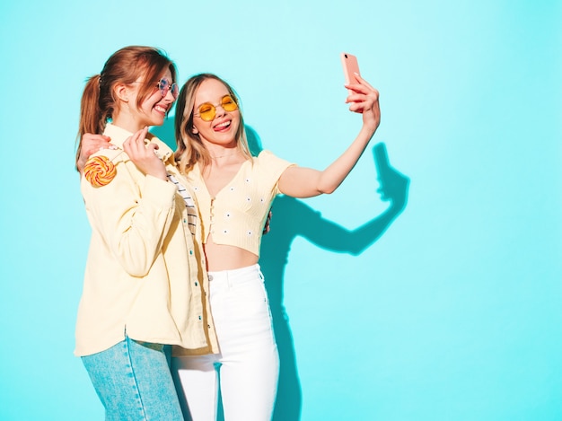 Two young beautiful blond smiling hipster female in trendy summer clothes