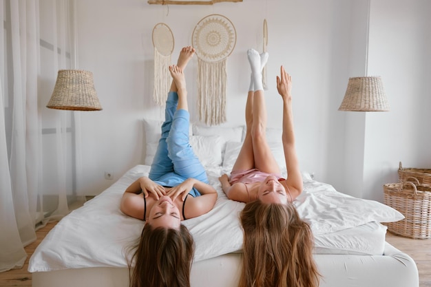 Two young beautiful girl friends on bed enjoying free time together